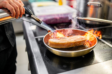 Professional chef cooking pork meat in frying pan on stove in restaurant kitchen