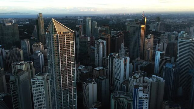Drone circling sunlit high-rise of Makati city, evening in Manila, Philippines
