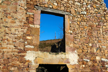 telecommunications antenna seen through the window on the stone and cement wall of a ruined house