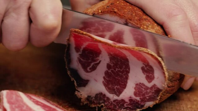 The chef slices a large piece of cured meat and shows how tender and tasty the ham is. Italian coppa, prosciutto