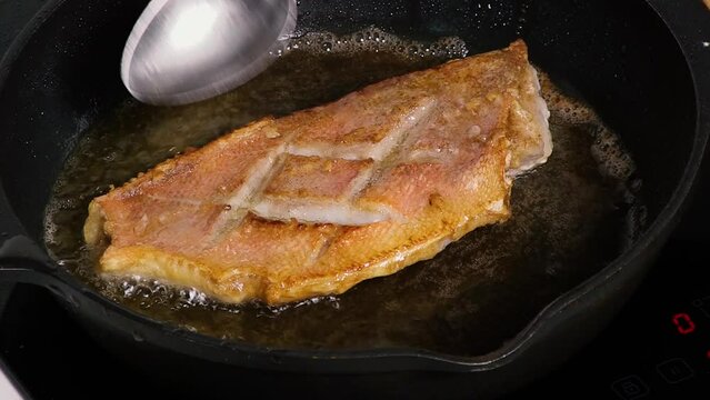 The chef fries a fillet of fish in a pan and pours oil over it