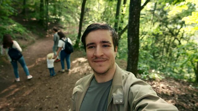 A man captures a self-portrait photograph in a wooded area.