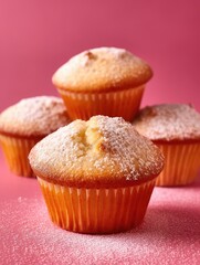 Four cupcakes with powdered sugar on a pink background.