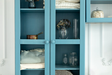 Wooden blue book case with decor and flowers in vase near wall in living room. Cozy home interior...