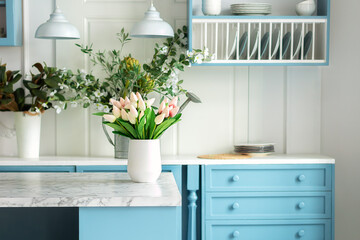 Kitchen island in dining room. Stylish cozy cuisine with tulips flowers in vase. Wooden kitchen in spring decor. Kitchen utensil, dishes and plate on shelves. Blue kitchen interior with furniture	
