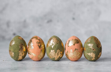 Stylish Easter eggs in peach Peach Fuzz and olive green with a coating of golden sweat on a gray background. The concept of happy Easter 2024.