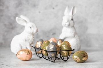 Stylish beautiful Easter eggs with golden potali coating and Easter bunny on a gray background. The...