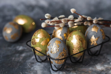 Stylish beautiful Easter eggs with golden enamel, willow branches and feathers on a gray...