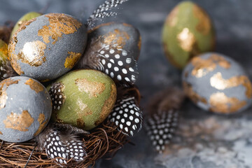 Stylish beautiful Easter eggs with a golden coating of sweat and feathers in a bird's nest of...