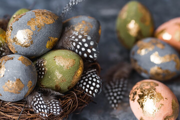 Obraz premium Stylish beautiful Easter eggs with a golden coating of sweat and feathers in a bird's nest of brushwood on a gray background. The concept of happy Easter 2024.
