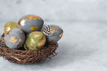 Stylish beautiful Easter eggs with a golden coating of sweat and feathers in a bird's nest of brushwood on a gray background. The concept of happy Easter 2024.