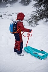 Portrait of a young European boy 7 - 9 years old in the warm winter jacket standing on the snowy winter background with sledge