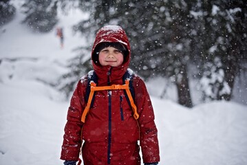 Portrait of a young European boy 7 - 9 years old in the warm winter jacket standing on the snowy winter background with sledge
