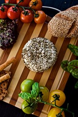 Healthy homemade cheese with Provencal herbs laying on the wooden board with tomatoes, basil, gluten free bread and salad 