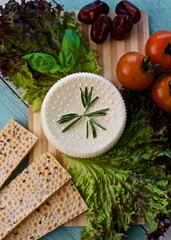 Flat lay of a healthy homemade cheese laying on the wooden board with tomatoes, basil, gluten free crispbreads and rosemary