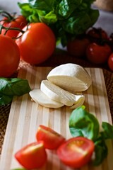Flat lay of healthy homemade mozzarella cheese, red tomatoes and basil laying on the wooden cutting board