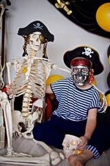 Young boy 7- 9 year old dressed as a pirate sitting on the floor with the pirate skeleton