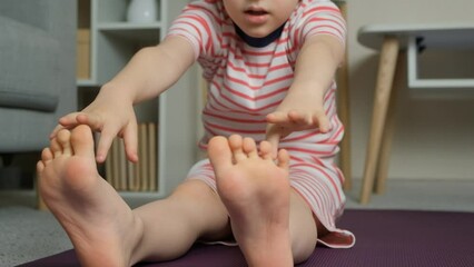 Child doing stretching exercises at home, trying to reach his toes with his hands while sitting. - Powered by Adobe
