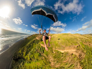 Extreme paragliding pilot soaring in the New Zealand beach at sunset. Adventure concept