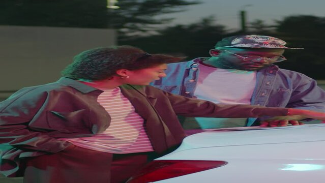 Vertical side full medium shot of African American fellow road trippers deciding on route studying country map on car hood at night