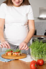 Pregnant young woman preparing healthy sandwiches with microgreens and vegetables. Food rich in fiber