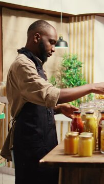 Vertical Video African american farmer opening local zero waste store with natural additives free bulk products and homegrown produce. Merchant preparing goods in reusable jars at eco supermarket