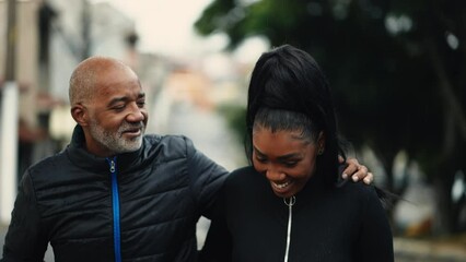 Joyful middle-aged dad talking with teenage daughter while strolling together in urban street outside. Father with arm around offspring walks forward while giving advice