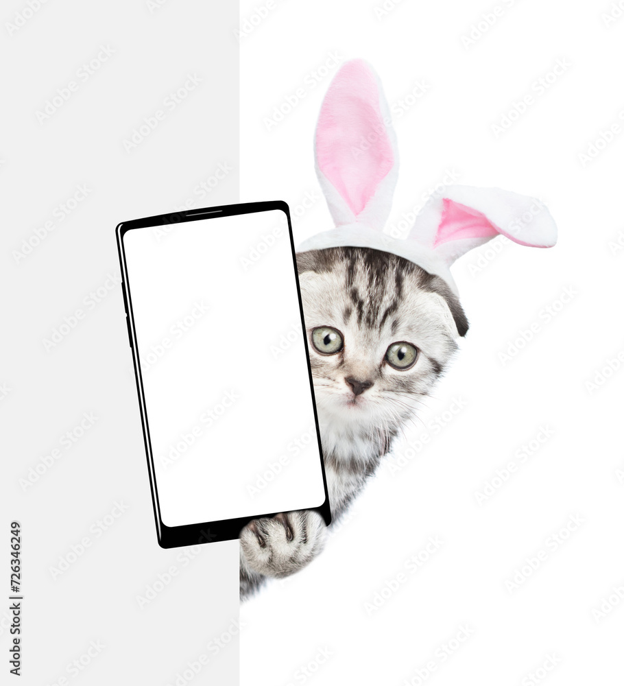 Aufkleber cute kitten wearing easter rabbits ears holds big smartphone with white blank screen and looks from 