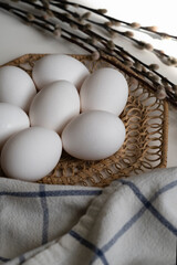 white chicken eggs lie on a brown wicker stand next to a willow branch, top view