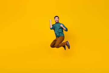 Fototapeta na wymiar Full length photo of overjoyed man dressed dotted shirt jumping win lottery clenching fists isolated on vibrant yellow color background