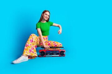 Full length photo of gorgeous woman dressed green top print trousers indicating at vintage boombox isolated on blue color background
