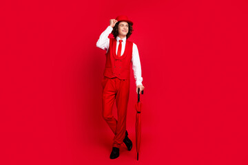 Full length photo of minded boyfriend prepared for a date in classic suit with umbrella looking novelty isolated on red color background