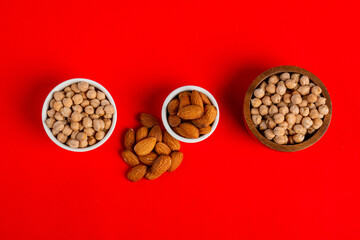 Chickpeas source and peeled barley and seed almonds in a basket wooden isolated on red background