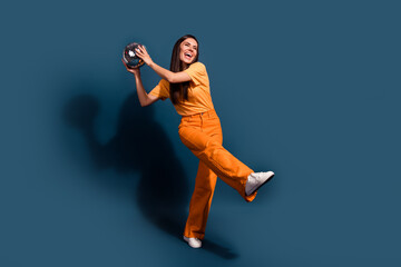 Fototapeta na wymiar Full body length photo of lady wear orange t shirt and pants hold shining disco ball at home party isolated on dark blue color background