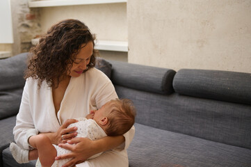 A happy affectionate mother holding a sleeping baby boy in her arms. Maternity leave lifestyle,...