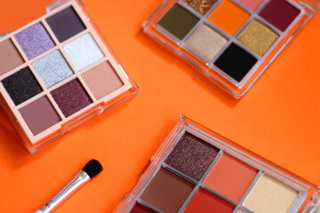 Colorful eyeshadow palettes and make up brush on orange background. Selective focus.