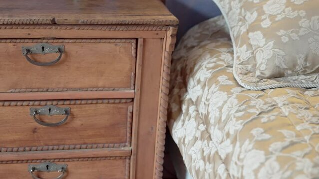 A close up of an antique wooden nightstand complementing the elegant and textured bedding in a cozy bedroom