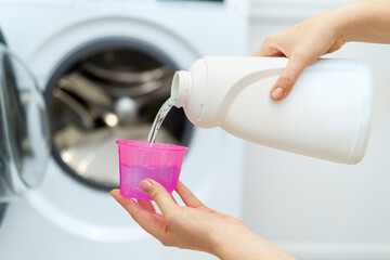 Person adding liquid laundry detergent to the washer, close up. Female hand holding laundry...