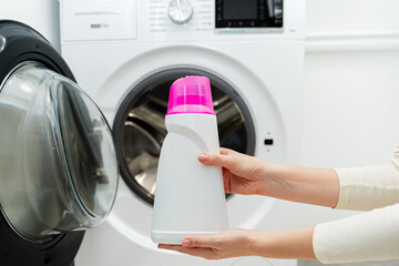 Person adding liquid laundry detergent to the washer, close up. Female hand holding laundry...