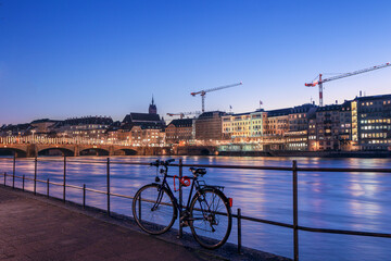 Fototapeta na wymiar A bike leaning on the river bank rails in the Swiss old city Basel with the Mittler Bridge at the background with Christmas light illumination in blue hours.