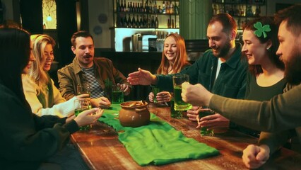 Wishing wealth and luck. Young happy people celebrating St Patrick's day at pub, drinking green beer, throwing golden coins into pot. Concept of leisure time, friendship, fun and joy, youth, enjoyment