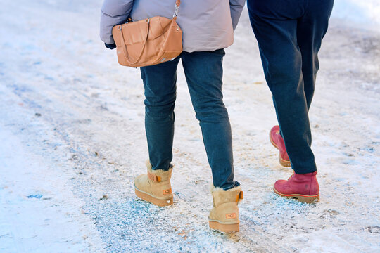 Minsk, Belarus.Jan 21, 2024. Women legs in warm UGG boots, ankle boots closeup, women walking on snowy road. Woman in warm clothes walking on sidewalk covered with snow in winter day. Selective focus