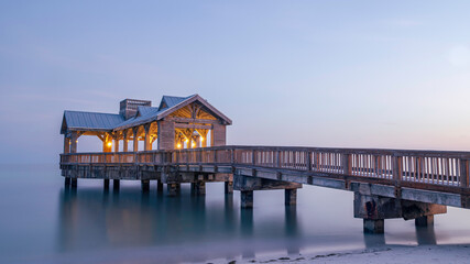 Wooden pier, located in Key West, Florida, reaching out into very calm tropical waters at sunset.  There are lights on the structure, as the sky goes dark.