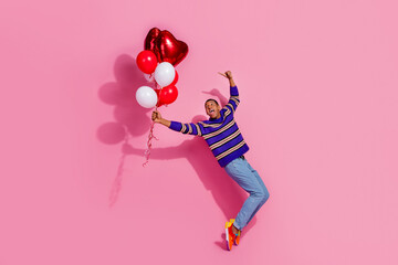Full length photo of funky funny man wear striped sweater showing finger pointing heart balloons bouquet isolated pink color background