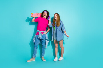 Full body photo of young couple teenagers boyfriend with girlfriend hobby penny board talking old phone isolated on cyan color background