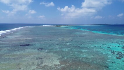 Drone view of paradise islands of the Maldives with coral reefs under the waves of blue the Indian Ocean.