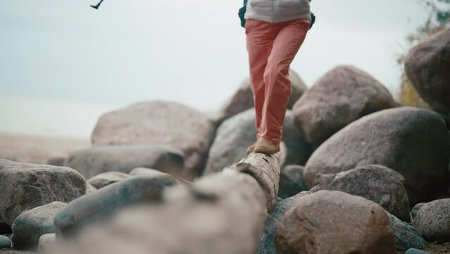 Legs of an elderly traveler walking through the forest. Senior woman walking on a tree root in the forest. Close up hiker walk. Follow adventurer in wild location. Outdoor activity, journey concept.
