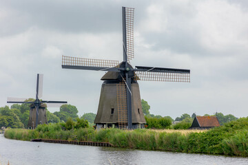 Summer landscape, Traditional Dutch windmills Molenkade under white grey cloudy sky, Polder land with small canal or ditch along the road, Countryside of Netherlands, Alkmaar Noord, North Holland.
