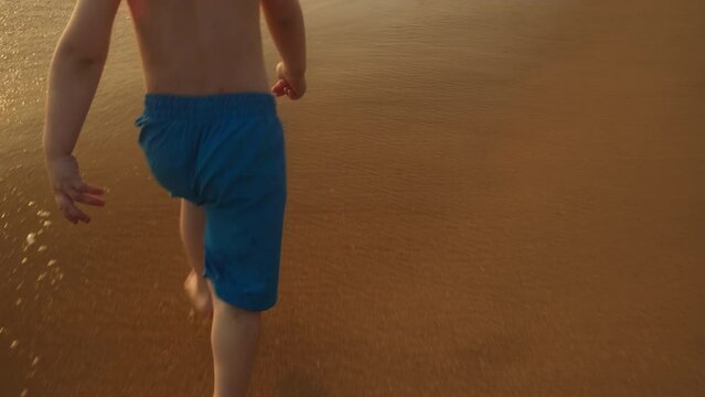 Beach holidays. Little boy runs barefoot along ocean coast.