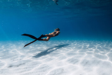 Woman freediver swimming underwater in blue sea over sandy bottom. Female swims with fins undersea